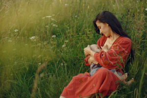 Mother with cute daughter. Mom breastfeeding her little son. Woman in a red dress.